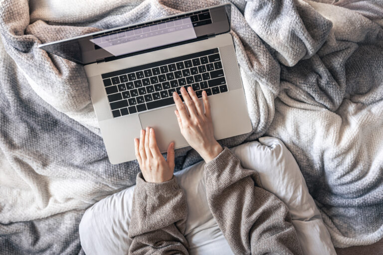 a woman working on a laptop while lying in bed, top view.