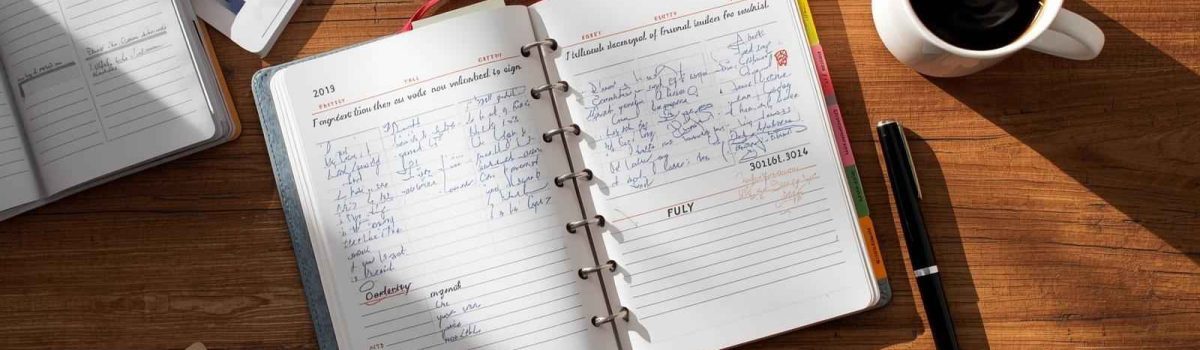 Open daily planner on wooden desk with handwritten schedule and coffee cup nearby